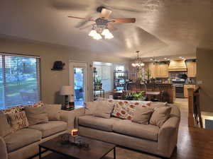 Living area featuring a textured ceiling, vaulted ceiling, ceiling fan, light wood-style floors, and a chandelier