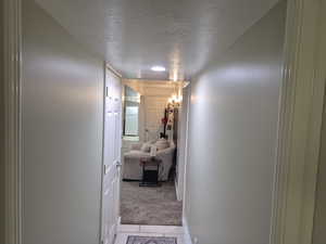 Hall with a textured ceiling, light colored carpet, and light tile patterned floors
