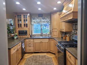 Kitchen with appliances with stainless steel finishes, custom exhaust hood, dark stone counters, recessed lighting, and glass insert cabinets