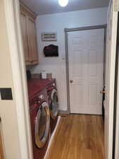 Washroom with light wood-style flooring, independent washer and dryer, cabinet space, and a textured ceiling