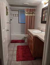 Bathroom with light tile patterned floors, shower / bathtub combination with curtain, vanity, and a textured ceiling