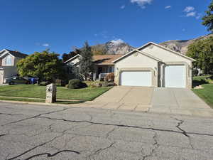 Ranch-style home featuring a front yard, a mountain view, a garage, driveway, and stucco siding