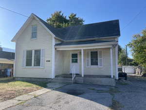 View of front of property featuring a shingled roof, a porch, and a storage shed