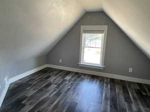 Additional living space featuring vaulted ceiling and dark wood-style flooring