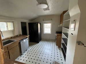 Kitchen with stainless steel appliances, light flooring, brown cabinets, lofted ceiling, and a textured ceiling