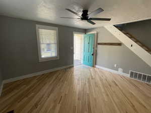 Unfurnished living room with a textured ceiling, light wood finished floors, and a ceiling fan