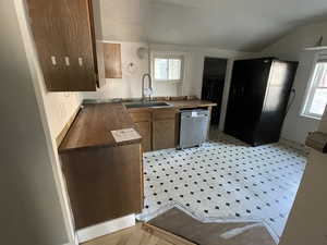 Kitchen with freestanding refrigerator, dishwasher, vaulted ceiling, brown cabinetry, and wooden counters
