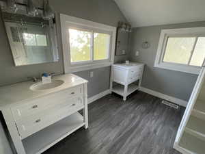 Bathroom featuring two vanities, dark wood-style flooring, vaulted ceiling, and a shower stall