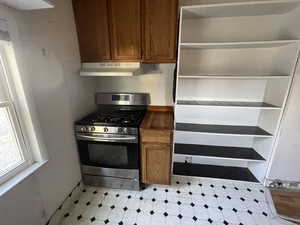 Kitchen featuring stainless steel range with gas cooktop, brown cabinets, under cabinet range hood, and light flooring