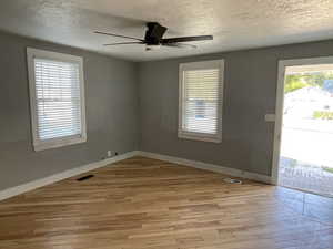 Empty room with a textured ceiling, light wood-style flooring, and ceiling fan