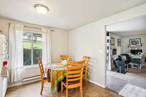 Dining space featuring baseboard heating, a textured ceiling, light colored carpet, and a desk