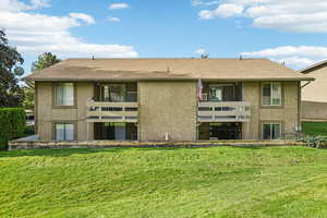 Back of house with a lawn, stucco siding, and a balcony