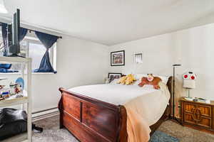Carpeted bedroom featuring baseboard heating and a textured ceiling