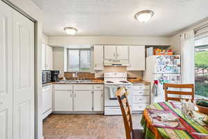 Kitchen with white appliances, white cabinetry, a textured ceiling, plenty of natural light, and under cabinet range hood