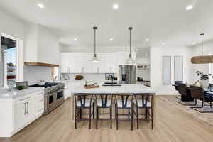 Kitchen featuring high quality appliances, a breakfast bar, light wood finished floors, light stone counters, and recessed lighting