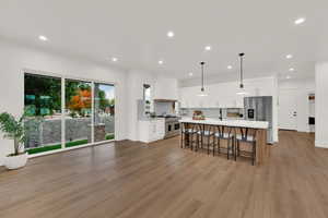 Kitchen featuring white cabinets, a center island with sink, recessed lighting, a breakfast bar, and hanging light fixtures
