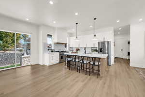 Kitchen with backsplash, an island with sink, a kitchen bar, white cabinetry, and recessed lighting