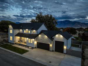 Modern farmhouse style home with a gate, driveway, stone siding, roof with shingles, and a porch