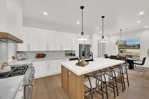 Kitchen with a breakfast bar area, light wood finished floors, pendant lighting, white cabinetry, and recessed lighting