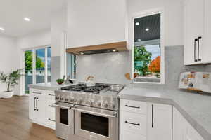 Kitchen with white cabinets, double oven range, light stone countertops, backsplash, and recessed lighting