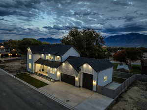 Modern farmhouse featuring stone siding, a mountain view, driveway, roof with shingles, and an attached garage