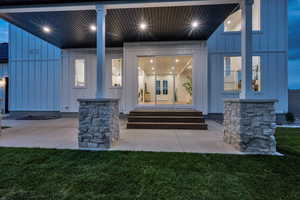 Exterior entry at twilight with board and batten siding, a patio area, and a yard