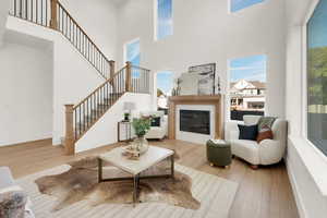 Living room with wood finished floors, a glass covered fireplace, a towering ceiling, and stairway