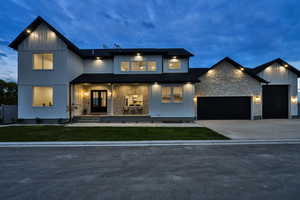 Modern inspired farmhouse with covered porch, stone siding, concrete driveway, a garage, and a front lawn