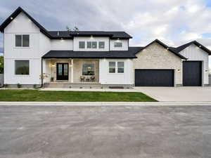 Modern farmhouse style home with a porch, board and batten siding, driveway, roof with shingles, and stone siding