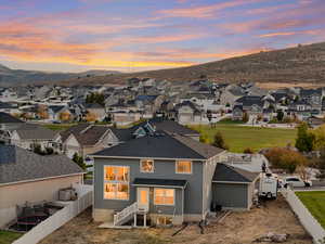 Back of house at dusk with stucco siding, a fenced backyard, a mountain view, and roof with shingles