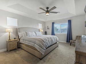Primary Bedroom featuring a tray ceiling, carpet, and ceiling fan