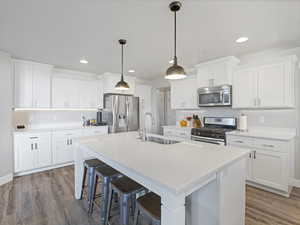 Kitchen with a kitchen bar, appliances with stainless steel finishes, white cabinetry, decorative light fixtures, and a kitchen island with sink