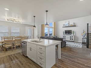 Kitchen featuring open floor plan, a center island with sink, pendant lighting, white cabinetry, and a kitchen breakfast bar