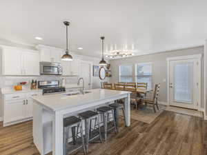 Kitchen with a breakfast bar, appliances with stainless steel finishes, hanging light fixtures, white cabinetry, and dark wood-style flooring