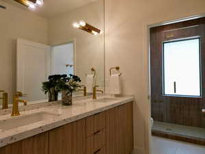 Full bath with double vanity, a shower stall, and light tile patterned flooring