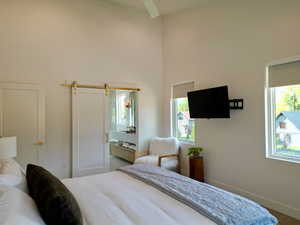 Bedroom featuring a barn door, ensuite bath, and a high ceiling