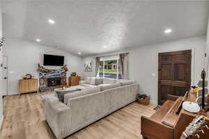 Living area with recessed lighting, light wood-type flooring, a fireplace, vaulted ceiling, and a textured ceiling