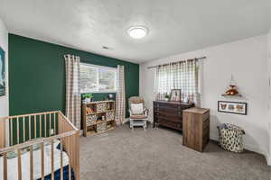 Carpeted bedroom with a nursery area and a textured ceiling