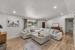 Living area featuring lofted ceiling, recessed lighting, light wood-style floors, and a textured ceiling