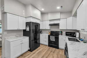 Kitchen featuring black appliances, light wood-style flooring, white cabinets, lofted ceiling, and light stone countertops