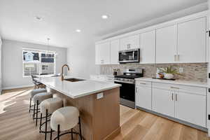 Kitchen with stainless steel appliances, white cabinets, a kitchen breakfast bar, a kitchen island with sink, and decorative light fixtures