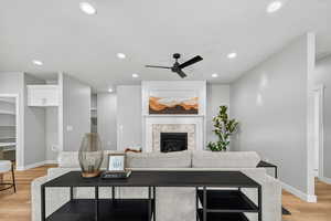 Living area with light wood-style flooring, a ceiling fan, recessed lighting, and a fireplace