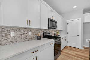 Kitchen featuring stainless steel appliances, tasteful backsplash, white cabinetry, light wood finished floors, and light stone countertops