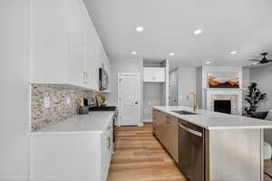 Kitchen with appliances with stainless steel finishes, a fireplace, a center island with sink, backsplash, and white cabinetry