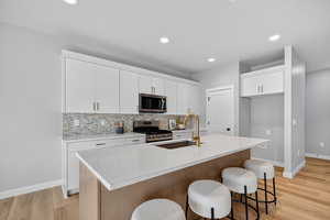 Kitchen with light wood-style floors, a kitchen island with sink, backsplash, a kitchen bar, and appliances with stainless steel finishes