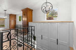 Hall with a chandelier, light wood finished floors, plenty of natural light, a textured ceiling, and an upstairs landing