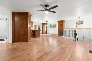 Unfurnished living room with light wood-style flooring, a chandelier, a textured ceiling, wine cooler, and ceiling fan
