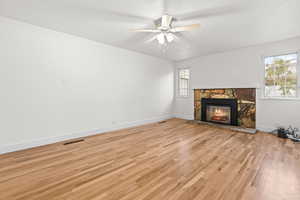 primary room with light wood-style flooring, a stone fireplace, and a ceiling fan