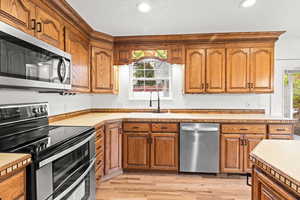 Kitchen featuring stainless steel appliances, light wood finished floors, light countertops, brown cabinetry, and recessed lighting
