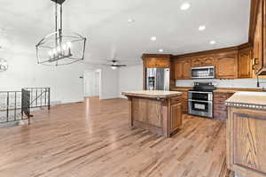 Kitchen with a kitchen island, appliances with stainless steel finishes, a ceiling fan, a breakfast bar area, and decorative light fixtures